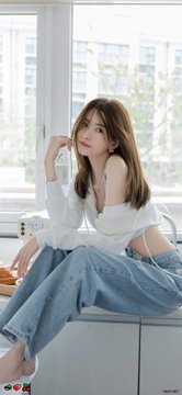 A young woman with long brown hair sits on a windowsill in a white off-shoulder top and blue jeans, looking at the camera.