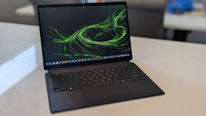 A sleek black laptop sits open on a white desk, displaying a vibrant green swirling abstract wallpaper with a dock of app icons at the bottom of the screen. The visible taskbar shows what appears to be a Linux-based desktop environment, hinting at the user's custom setup referenced in the post about migrating from closed ecosystems to a more intuitive distro.