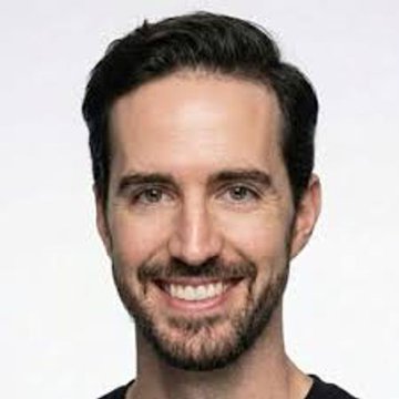 A headshot portrait of a smiling man with dark hair and a beard against a plain white background.