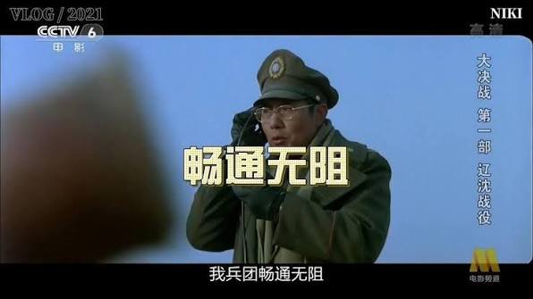 The image is a screenshot from a 2021 CCTV-6 broadcast of the Chinese film "大决战第一部：辽沈战役" (The Great Decisive Battle Part 1: Liaoshen Campaign), showing a man in a military uniform and cap holding binoculars, with the yellow subtitle "畅通无阻" and the white subtitle "我兵团畅通无阻" at the bottom. The accompanying post about crypto savings and mining APRs has no apparent connection to this historical war film scene.