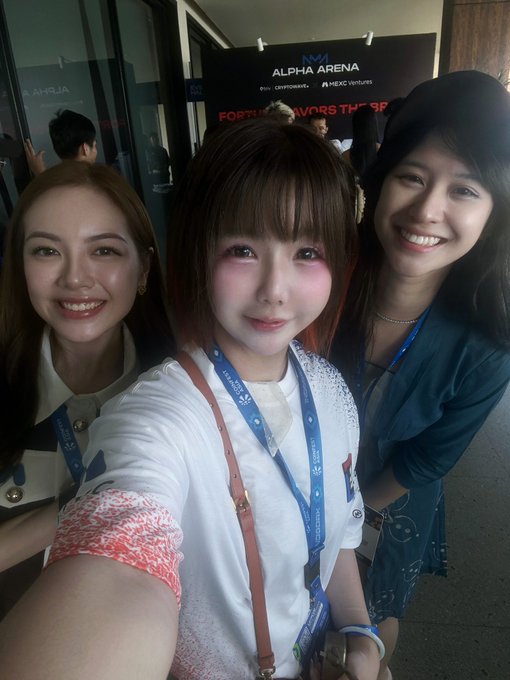 A selfie of three smiling young women at 'ALPHA ARENA' event featuring 'CRYPTOPUNKS' and 'NEXT VENTURES' branding, with 'FORTUNE FAVORS THE BOLD' visible on a banner.