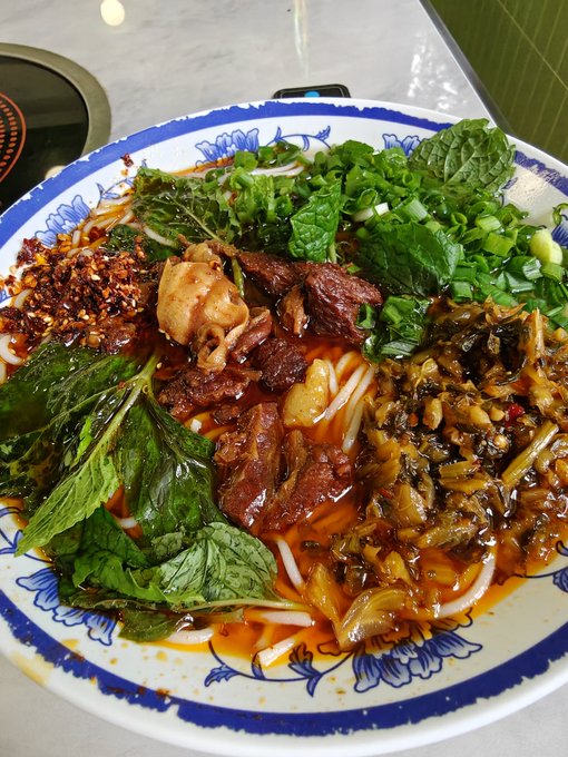 A bowl of Chinese-style beef noodle soup, likely Guilin rice noodles, is served with braised beef, chili flakes, pickled greens, and fresh mint and scallions in a rich red broth, fitting the casual breakfast outing ("Run out to eat breakfast, 1.5u") described in the post.