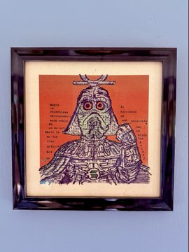 A framed artwork hangs on a blue wall, showing a stylized illustrated figure or mask with a red-orange background and dense handwritten markings.
