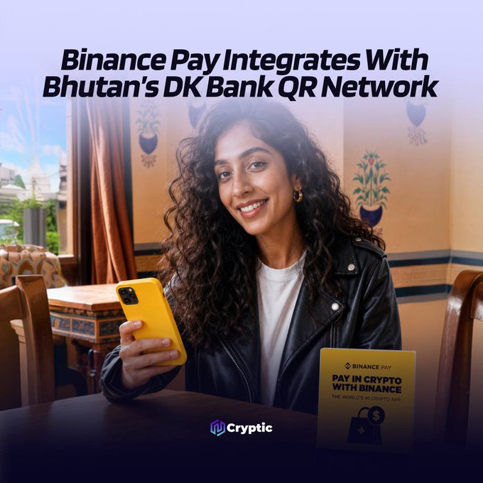 A woman in a leather jacket smiles while holding a yellow phone, with a Binance Pay "Pay in Crypto with Binance" sign displayed beside her, illustrating the new integration between Binance Pay and DK Bank's QR payment network enabling crypto payments at Bhutan's merchants. The image directly visualizes the announcement's use case of scanning QR codes through the Binance app to make crypto purchases.