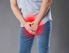 A person wearing a gray t-shirt and blue jeans clutches their lower abdomen and pelvic area, with a red highlight indicating pain or discomfort in that region.