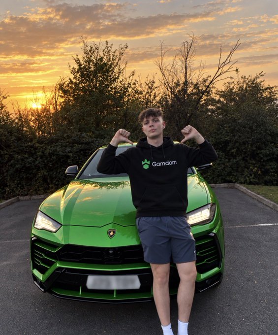 A young man wearing a black "Gamdom" hoodie poses with flexed arms in front of a green Lamborghini Urus at sunset. The image serves as promotional content for a $20 Gamdom giveaway, using the luxury car backdrop to attract engagement and entrants to the social media contest.