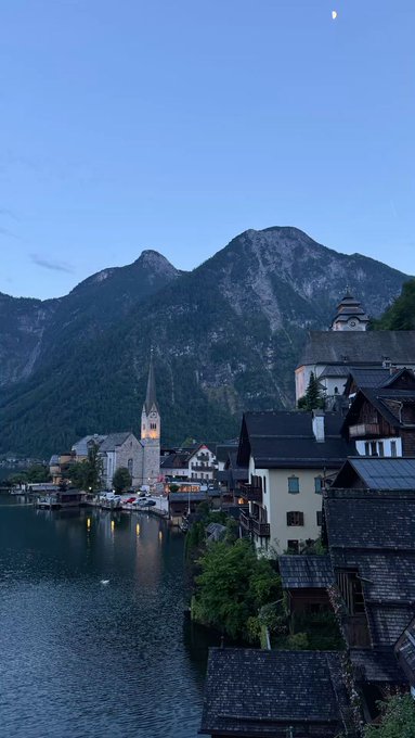 llor, a small town with white and gray buildings, sits on the banks of Lake Constance, surrounded by lush green mountains under a clear blue sky.