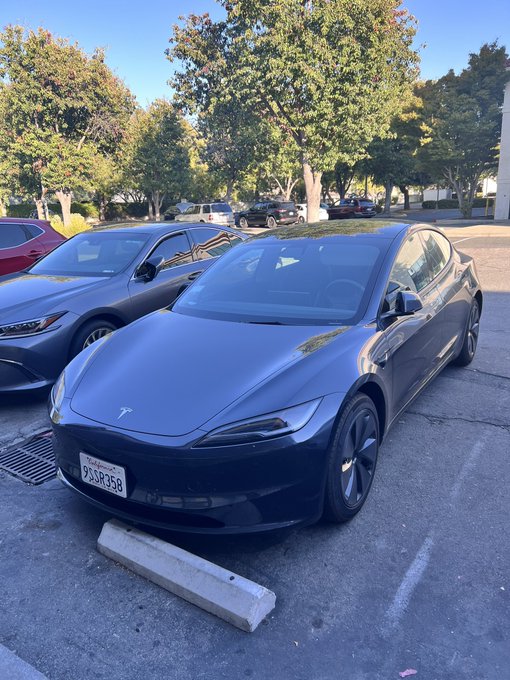 A black Tesla car with license plate 9SSP358 is parked in a lot next to other vehicles.