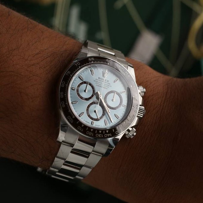A Rolex Cosmograph Daytona watch with an ice-blue dial rests on a wrist, displaying text such as "ROLEX," "OYSTER PERPETUAL," "SUPERLATIVE CHRONOMETER," and "DAYTONA," along with the tachymeter scale on its black ceramic bezel. The image illustrates the caption's point about platinum's subtle sheen, as the watch's platinum case reveals its understated luster only when viewed up close.