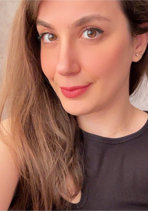 A woman with long brown hair takes a soft, warm-lit selfie, her subtle smile complementing the post's promotion of her NFT artwork "Wildfire 1/1 170 TEZ" from her "Artist vs Art" collection.