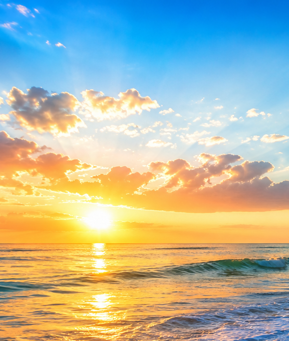 A scenic ocean sunset with golden sunlight reflecting on calm waters, scattered clouds, and a small wave breaking on the right.