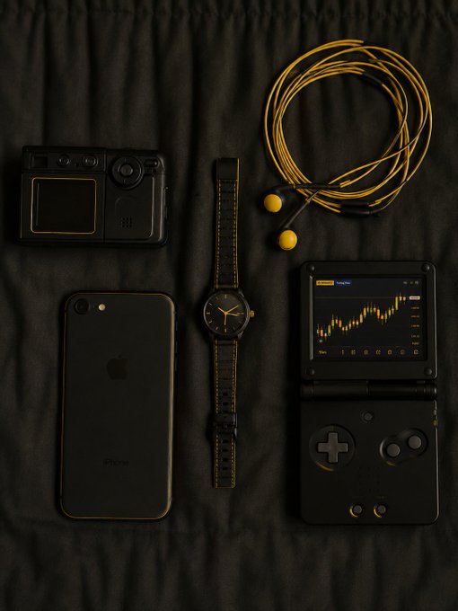 A flat-lay photograph on a black sheet showing several customized electronics with yellow accents: a handheld camera, an iPhone, a watch with a striped strap, earphones, and a handheld gaming console displaying a stock chart.