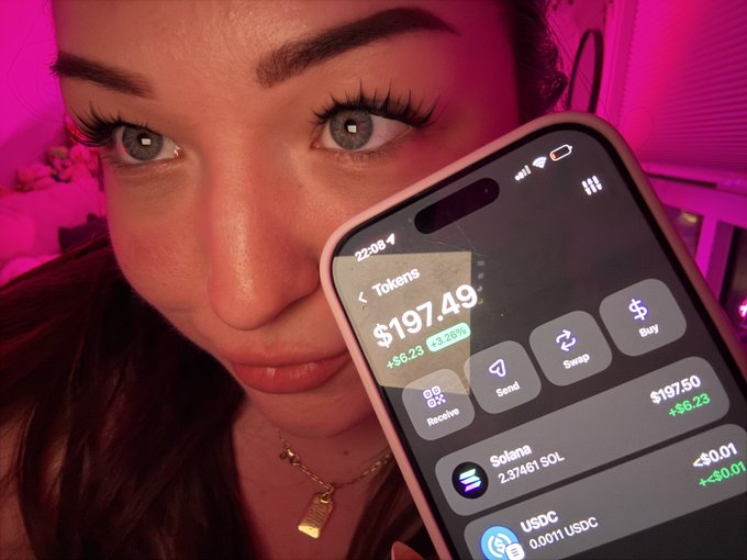 A woman holds up a phone displaying a crypto wallet showing $197.49 in tokens, including 2.37461 SOL worth just under $197.50, illustrating the accumulated Solana holdings from her daily $1 buying streak on day 226.