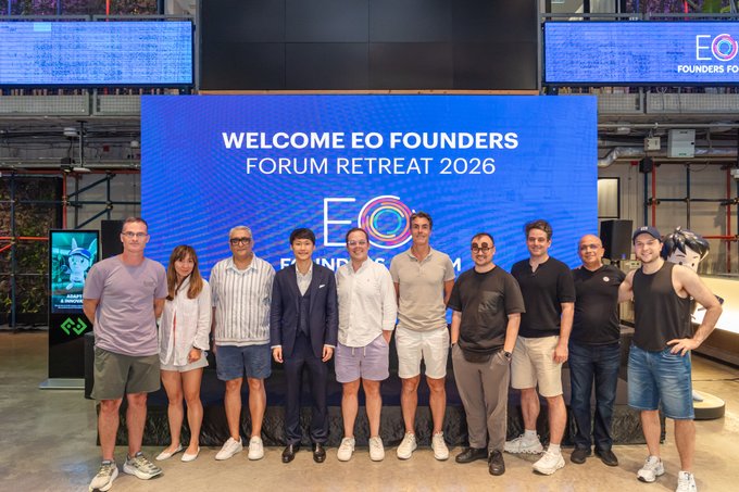 A group photo at the 'WELCOME EO FOUNDERS FORUM RETREAT 2026' event with attendees posing in front of a large branded display screen.