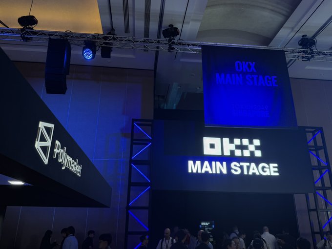 An event space features illuminated 'OKX MAIN STAGE' and 'Polymarket' signage hanging from the ceiling with blue lighting.