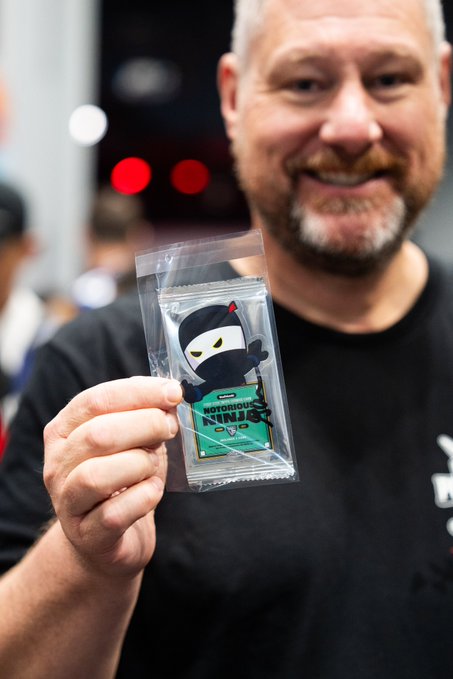 A smiling bald man with a goatee holds up a sealed plastic package containing a 'Notorious Ninja' sticker featuring a black ninja character.