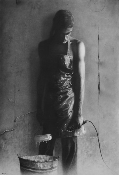 A moody black-and-white photograph of a person wearing a paint-splattered apron, holding a paint roller dripping paint into a bucket against a textured wall.