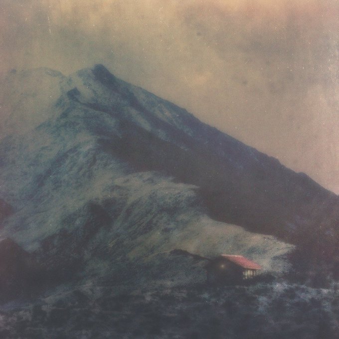 A moody painting depicts a large blue-gray mountain under a cloudy sky, with a small red-roofed structure visible at its base.