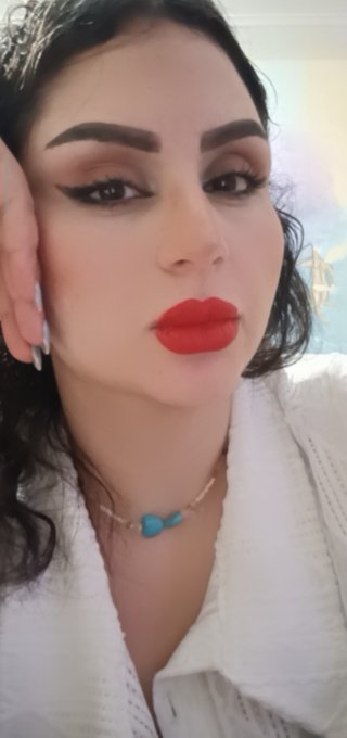 A close-up portrait shows a woman with dark hair, dramatic eye makeup, and bright red lipstick, wearing a white top and a delicate beaded necklace with a turquoise pendant.