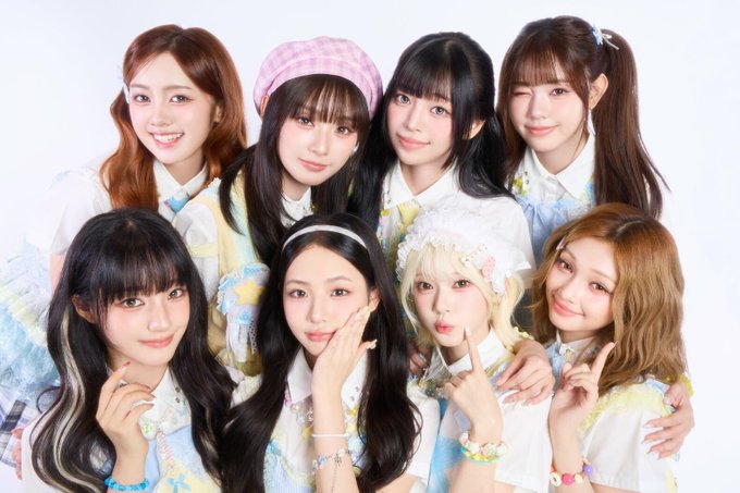Group photo of seven young women posing together in light, frilly pastel outfits with hair accessories against a white background.