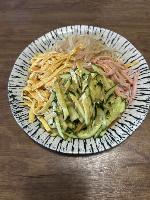 A plate of homemade hiyashi chuka (cold ramen noodles) topped with shredded cucumber, egg, ham, and bean sprouts sits on a wooden table, accompanied by the caption noting it was made the night before with two servings of noodles filling the maker up despite taking 30 minutes to prepare.