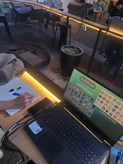 A person wearing a beanie works in a café on a laptop displaying "CRYPTOPUNKS" and "CRYPTOTITTIES" NFT collections in Persian, reflecting the "Art, NFTs until I die" theme. The scene captures the intersection of digital art creation and crypto culture in a casual workspace setting.