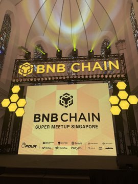 Illuminated stage sign at 'BNB CHAIN SUPER MEETUP SINGAPORE' with the text 'BNB CHAIN' flanked by honeycomb logos and sponsor logos below.