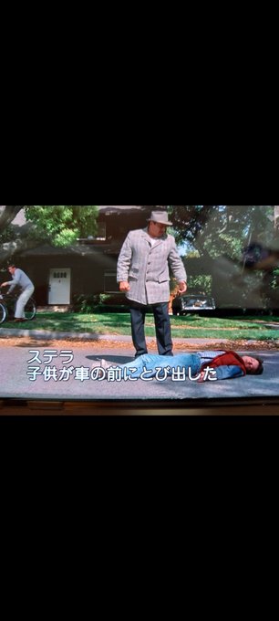In this image, there are two people standing next to each other with one person lying down on the ground while the other person stands over them. They appear to be engaged in a conversation or interaction. The scene takes place outdoors, possibly at an event or gathering.