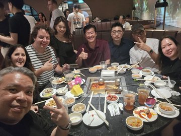 A group of people pose for a selfie around a table filled with various dishes and drinks at a restaurant.