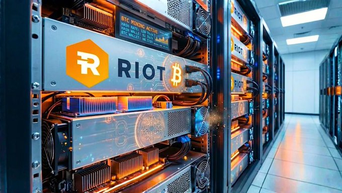 A row of illuminated Bitcoin mining rigs labeled "RIOT" with the company's orange logo and BTC symbol fills a high-tech data center aisle, visually underscoring Riot's reported sale of 4,300 BTC to fund its AI-driven compute buildout.