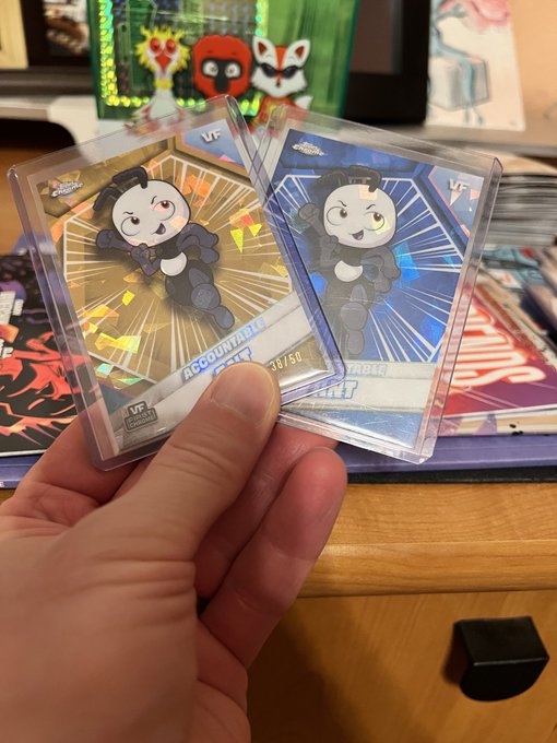 A hand holds two trading cards featuring a cartoon character in a black outfit with sunglasses; one card is gold ('ACCOUNTABLE' 30/50) and the other is blue ('RARE').