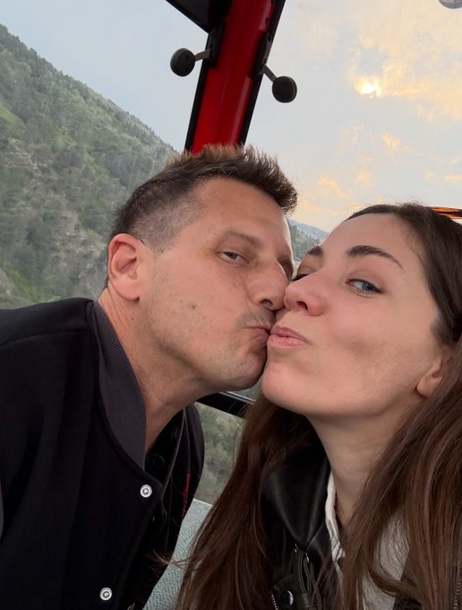 A couple shares a romantic kiss on what appears to be a mountain overlook or ride, capturing an intimate anniversary moment with the sunset sky behind them, celebrating their relationship as mentioned in the post tagging @JasonTezos.