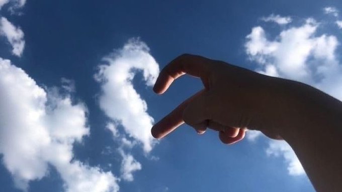 A hand reaches up toward a bright blue sky with scattered white clouds, creating the illusion of pinching or "picking" a cloud, symbolizing the post's reflection on simplifying content down to its essence rather than overloading with detailed analysis.