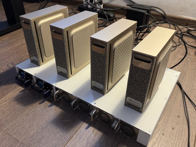 Four gold-colored external GPU enclosures connected to a shared mining/AI rig base with cooling fans, sitting on a wooden floor with cables in the background.