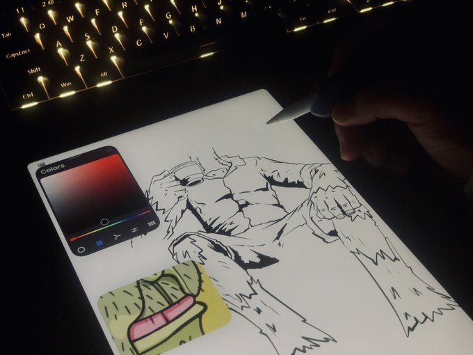 A photograph showing an artist using a stylus to draw a muscular anime/manga character in black ink on a tablet, with a color picker app visible and a lit keyboard in the background.