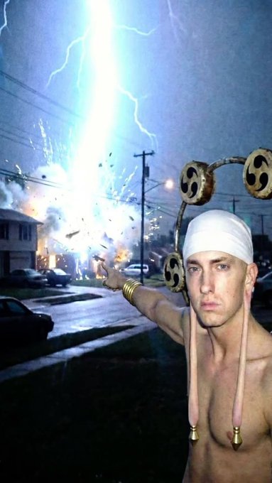 A man wearing a white headband with attached wooden wheels and tassels stands shirtless on a suburban street, pointing toward a bright explosion with lightning in the background.
