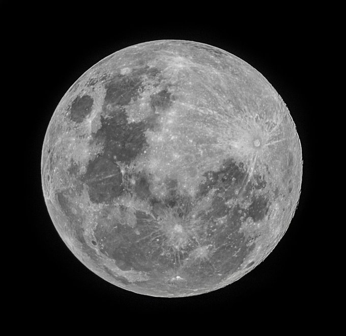 A detailed black and white photograph of the full moon showing craters and lunar surface features against a black sky.