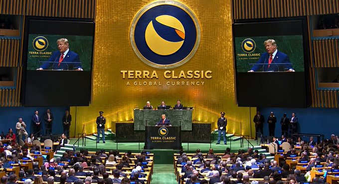 A wide shot of the Terra Classic 'A Global Currency' conference held in the United Nations General Assembly Hall, featuring Donald Trump speaking at the podium with his image displayed on the large gold backdrop screens.