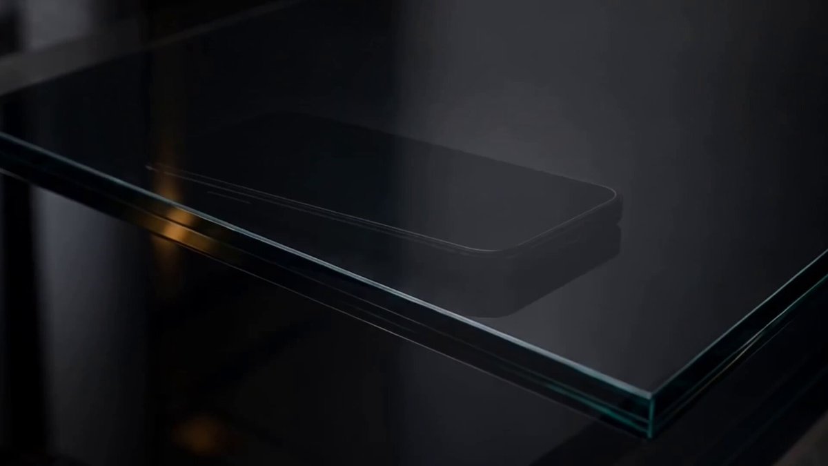 The image shows a glass table with a black cell phone placed on top of it, which appears to be an older model or a flip phone. The background features a dark color that contrasts with the clear glass surface of the table. The text "The world, thus opens up." is written in white at the bottom right corner of the image.