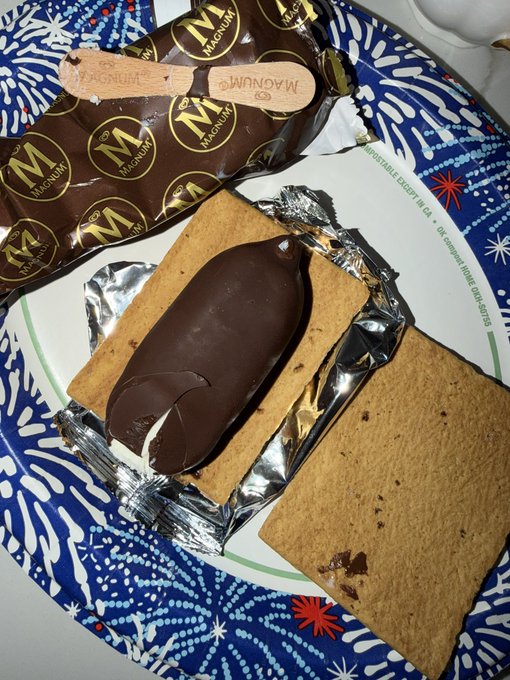Magnum ice cream sandwiches with chocolate ice cream bars resting on their graham cracker cookie halves, one still in foil packaging, on a blue patterned paper plate.
