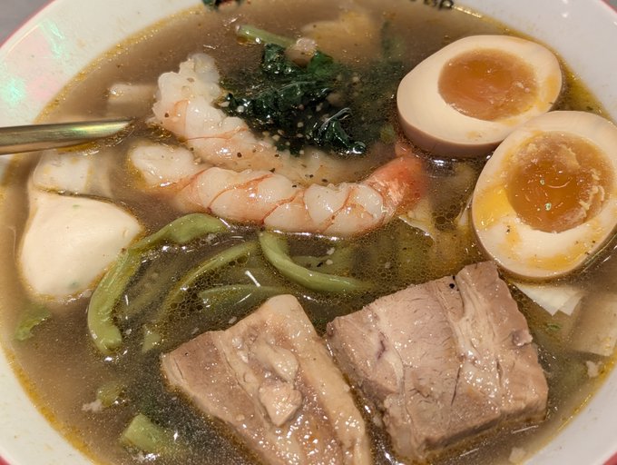 A steaming bowl of Sichuan-style hot pot features shrimp, soft-boiled egg halves with runny yolks, pork slices, green noodles, and dark greens in a spicy broth, visually mirroring the post's metaphor of the "spicy numbing" crypto market with its lingering heat and bold flavors.