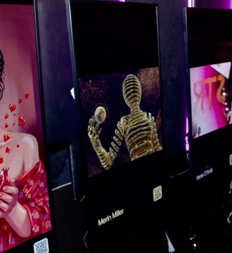 Three illuminated photo kiosks in a dark setting, with the center one displaying a golden skeleton holding a mirror, attributed to 'Mehdi Mascheri'.