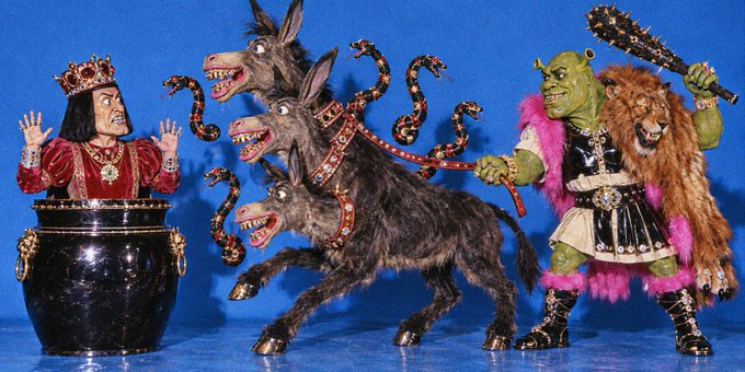 A collection of figurines depicting characters from the Shrek franchise, including Lord Farquaad emerging from a barrel, a multi-headed donkey (Donkey), and Shrek in gladiator attire alongside Puss in Boots.