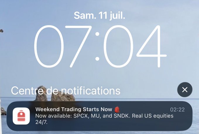 Phone lock screen displaying the time '07:04' on 'Sam. 11 juil.' (Saturday, July 11), with a notification from a trading app reading 'Weekend Trading Starts Now - Now available: SPCX, MU, and SNDK. Real US equities 24/7.'