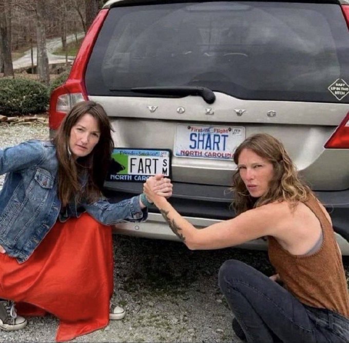 Two women pose in front of a Volvo SUV with North Carolina license plates, one reading 'FART' and the other 'SWART', both making exaggerated disgusted expressions.