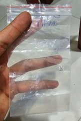 A hand holds a small clear plastic bag containing two diamond-like stones with handwritten markings including '9.10' on the bag.