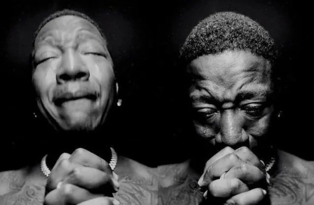 A dramatic black-and-white image shows two men with their eyes closed and hands clasped together in apparent prayer.