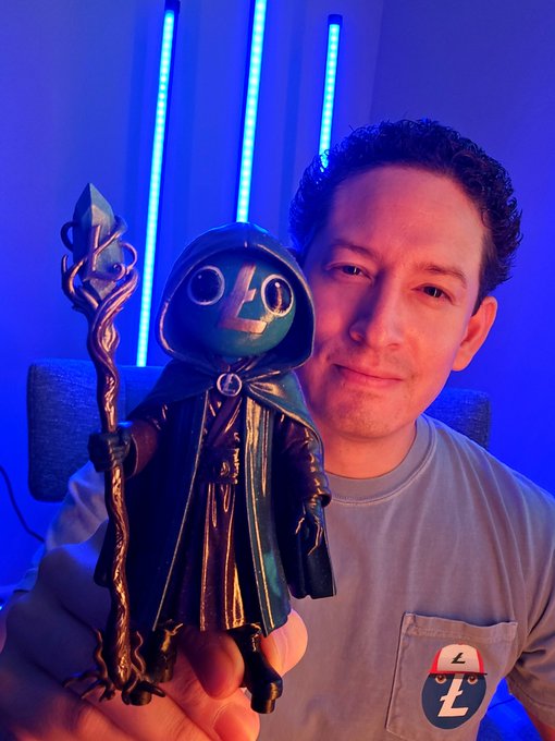 A man in a grey t-shirt with a 'Z' logo holds up a hooded figurine with the number '40' on its face, illuminated by blue light bars in the background.