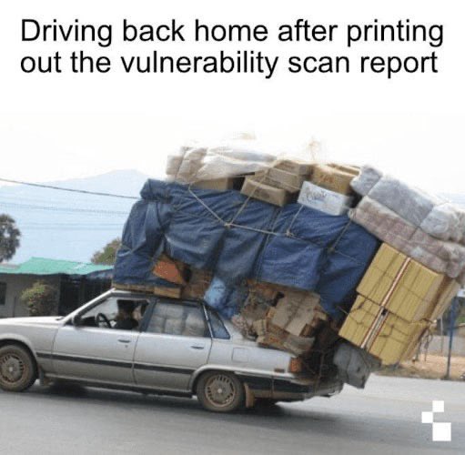 A silver sedan is severely overloaded with cardboard boxes and large tarp-wrapped bundles strapped precariously to its roof, with a caption reading 'Driving back home after printing out the vulnerability scan report.'