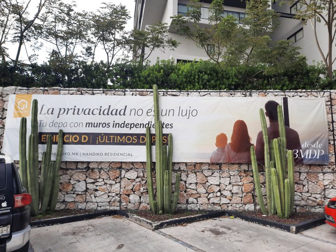 A billboard advertisement on a stone wall reads 'La privacidad no es un lujo. Tu depa con muros independientes desde $3MDP' for BMDP Handiko Residencial, partially obscured by cacti.